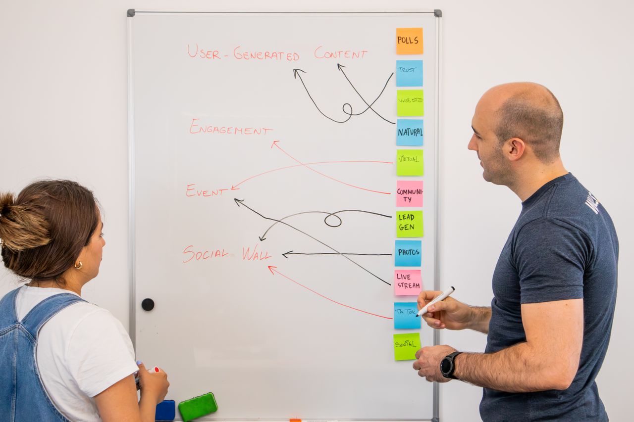 Two coworkers are sharing ideas at a whiteboard in a creative strategy meeting.